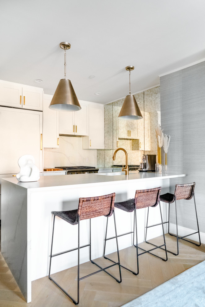 Design ideas for a contemporary open plan kitchen in New York with a drop-in sink, shaker cabinets, white cabinets, marble benchtops, white splashback, mirror splashback, stainless steel appliances, light hardwood floors, with island, beige floor and white benchtop.