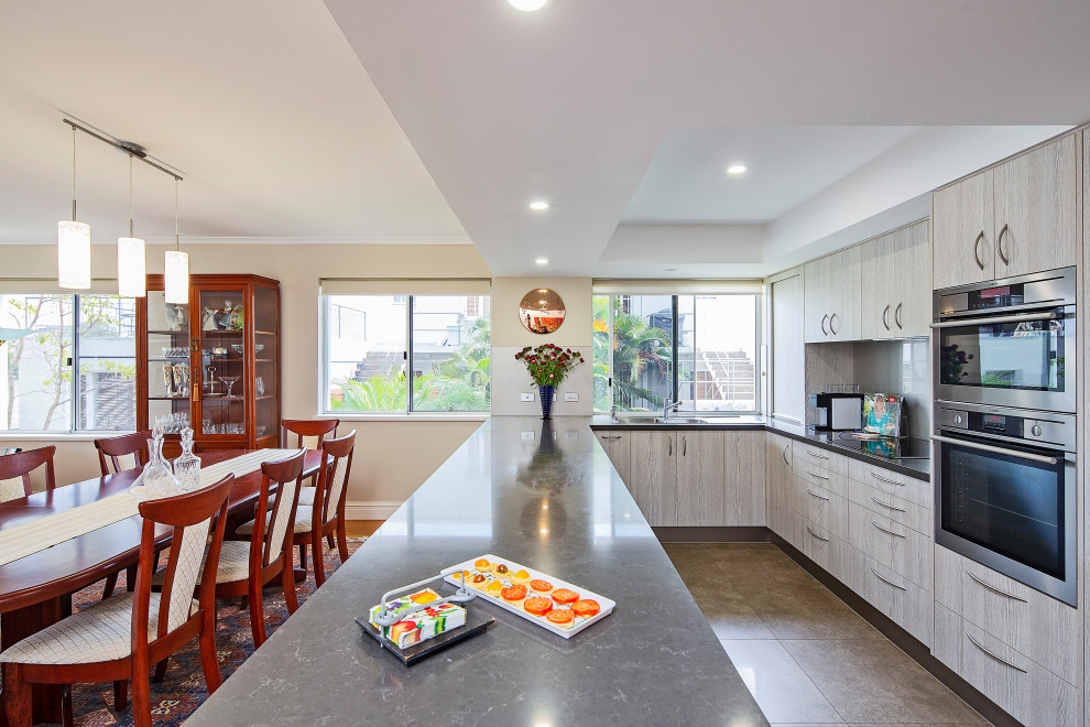 Photo of a medium sized contemporary u-shaped open plan kitchen in Brisbane with flat-panel cabinets, light wood cabinets, engineered stone countertops, glass sheet splashback, stainless steel appliances, medium hardwood flooring, a breakfast bar, brown floors, black worktops, a double-bowl sink, grey splashback and a drop ceiling.