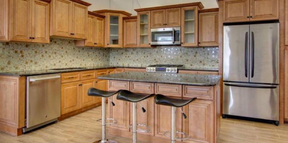 Open concept kitchen - transitional l-shaped porcelain tile and beige floor open concept kitchen idea with an undermount sink, raised-panel cabinets, medium tone wood cabinets, granite countertops, beige backsplash, ceramic backsplash, stainless steel appliances, an island and brown countertops