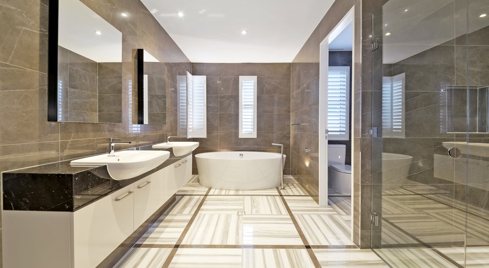 Photo of a contemporary master bathroom in Brisbane with flat-panel cabinets, white cabinets, a freestanding tub, an alcove shower, a two-piece toilet, gray tile, grey walls, an integrated sink, grey floor, a hinged shower door and black benchtops.