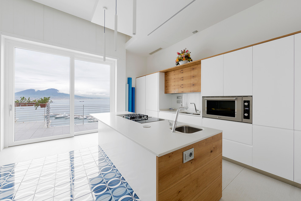 Inspiration for an expansive contemporary open plan kitchen in Naples with an undermount sink, flat-panel cabinets, light wood cabinets, quartz benchtops, white splashback, glass sheet splashback, stainless steel appliances, with island and white benchtop.