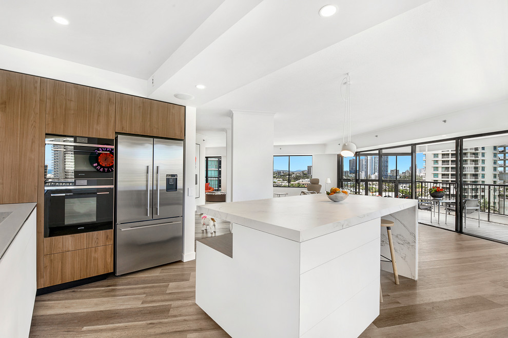 Photo of a large contemporary l-shaped open plan kitchen in Gold Coast - Tweed with flat-panel cabinets, medium wood cabinets, quartz benchtops, medium hardwood floors, with island, brown floor, stainless steel appliances and grey benchtop.