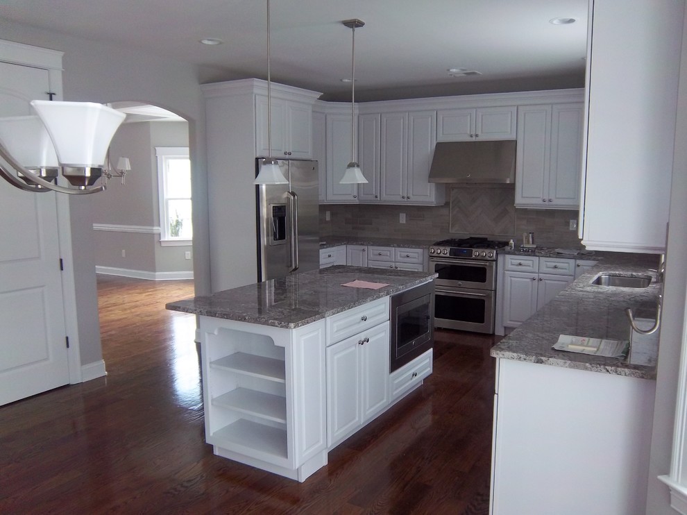 Kitchen - large transitional u-shaped dark wood floor and brown floor kitchen idea with an undermount sink, raised-panel cabinets, white cabinets, granite countertops, gray backsplash, porcelain backsplash, stainless steel appliances, an island and gray countertops