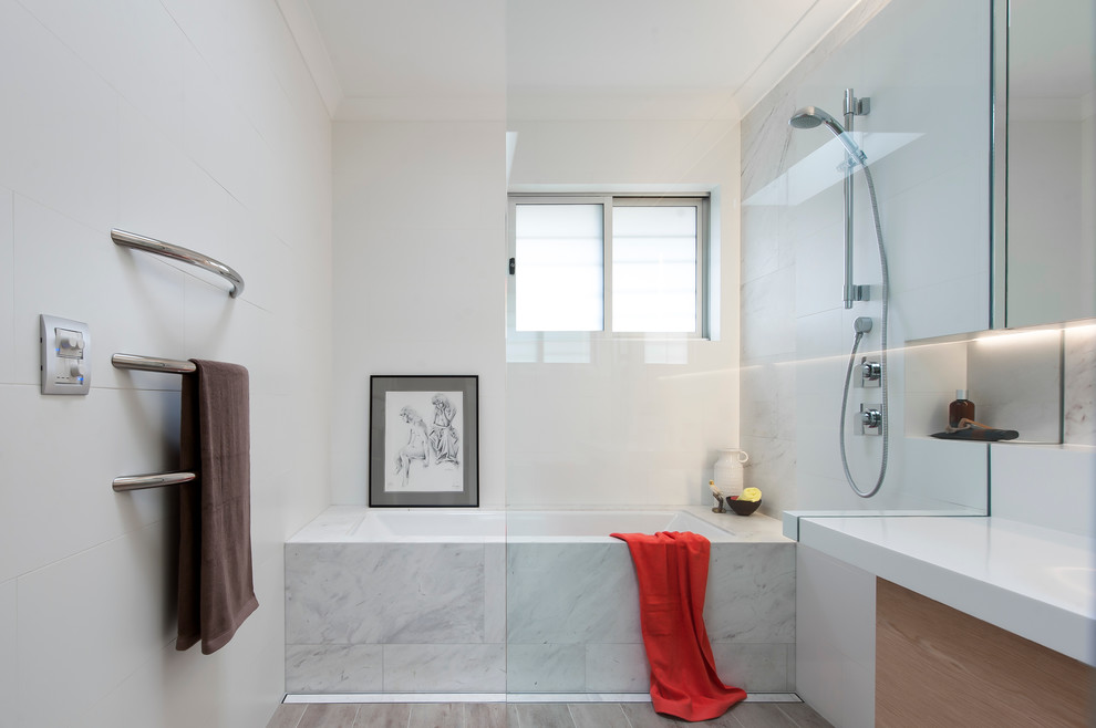 This is an example of a small contemporary 3/4 bathroom in Sydney with a wall-mount sink, light wood cabinets, solid surface benchtops, an undermount tub, an open shower, white tile, ceramic tile, white walls, ceramic floors, flat-panel cabinets and an open shower.