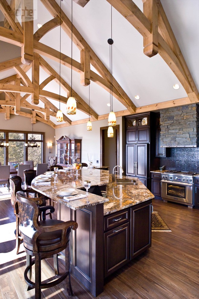 Large transitional l-shaped medium tone wood floor and brown floor eat-in kitchen photo with an undermount sink, raised-panel cabinets, dark wood cabinets, black backsplash, mosaic tile backsplash, stainless steel appliances, beige walls, an island and granite countertops