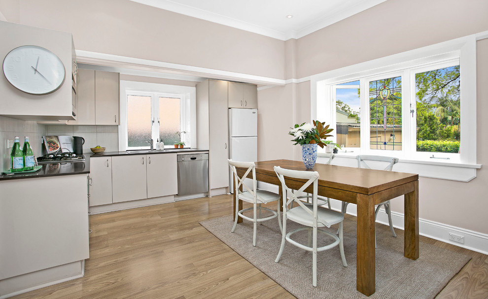 Small transitional l-shaped eat-in kitchen in Sydney with a double-bowl sink, beige cabinets, granite benchtops, beige splashback, ceramic splashback, stainless steel appliances and medium hardwood floors.