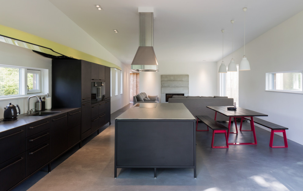 Large contemporary galley open plan kitchen in Oxfordshire with an undermount sink, flat-panel cabinets, black cabinets, panelled appliances, cement tiles, with island, grey floor and black benchtop.