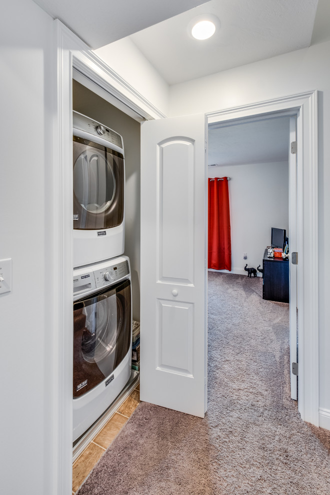 Small contemporary laundry cupboard in Other with grey walls, carpet, a stacked washer and dryer and beige floor.
