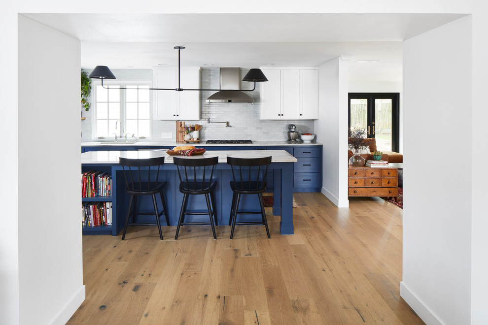 Inspiration for a large transitional l-shaped light wood floor and beige floor open concept kitchen remodel in Austin with an undermount sink, shaker cabinets, blue cabinets, marble countertops, white backsplash, subway tile backsplash, stainless steel appliances and an island