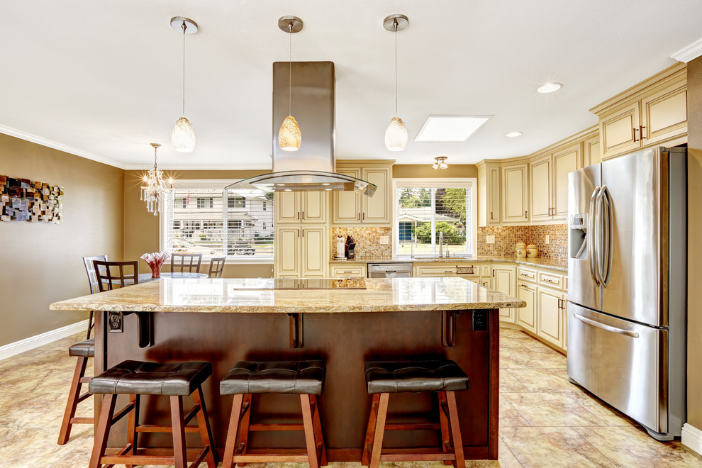 Photo of a mid-sized traditional l-shaped eat-in kitchen in DC Metro with a double-bowl sink, raised-panel cabinets, beige cabinets, granite benchtops, multi-coloured splashback, mosaic tile splashback, stainless steel appliances, vinyl floors, with island, beige floor and brown benchtop.
