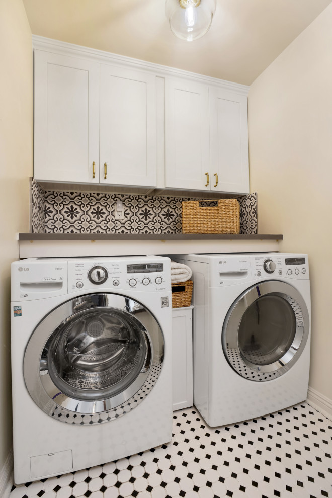 Large transitional l-shaped dedicated laundry room in Orange County with a single-bowl sink, shaker cabinets, white cabinets, quartz benchtops, white splashback, ceramic splashback, white walls, ceramic floors, a side-by-side washer and dryer, white floor and grey benchtop.