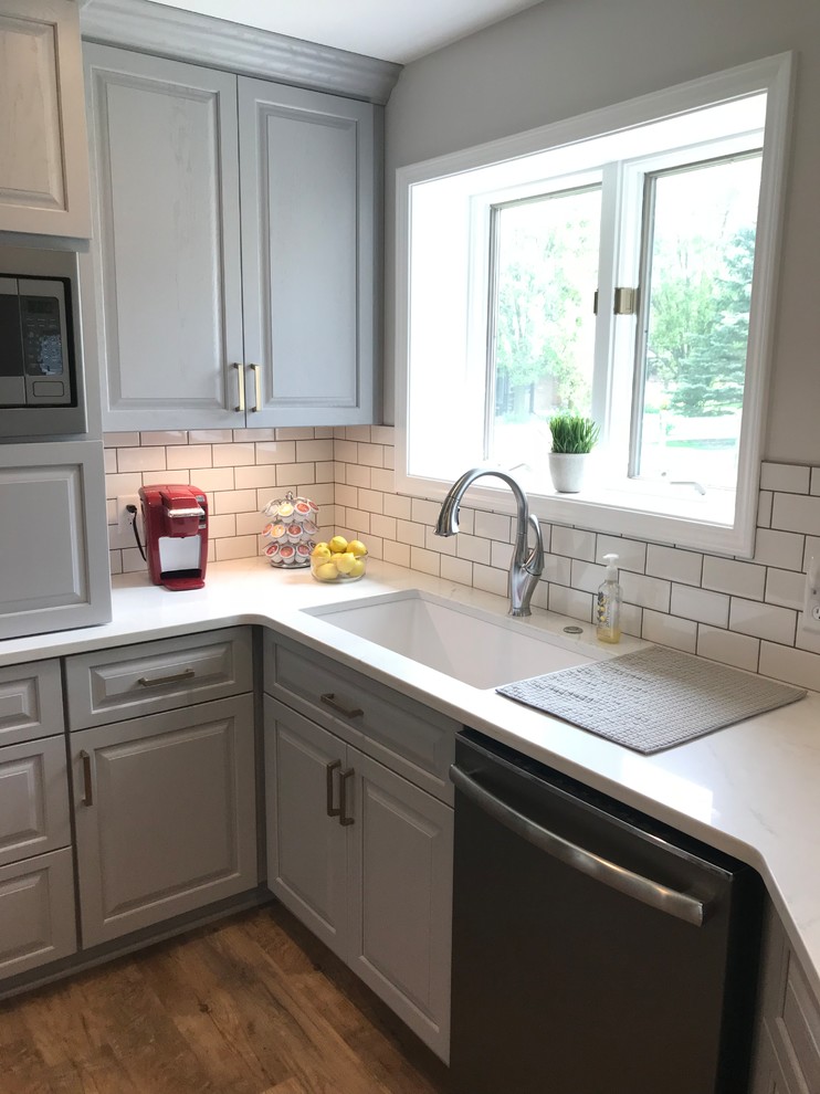Example of a mid-sized transitional u-shaped vinyl floor and brown floor enclosed kitchen design with an undermount sink, raised-panel cabinets, gray cabinets, quartz countertops, white backsplash, ceramic backsplash, a peninsula and white countertops