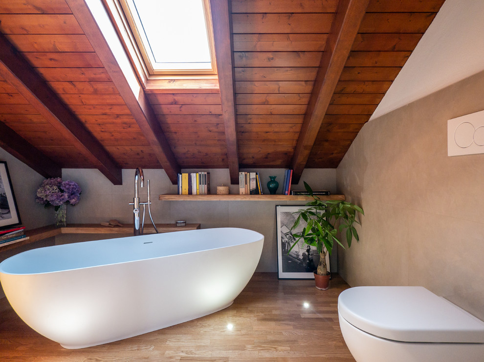 Inspiration for a mid-sized mediterranean master bathroom in Milan with light wood cabinets, a freestanding tub, a wall-mount toilet, beige tile, porcelain tile, white walls, light hardwood floors, a vessel sink and wood benchtops.
