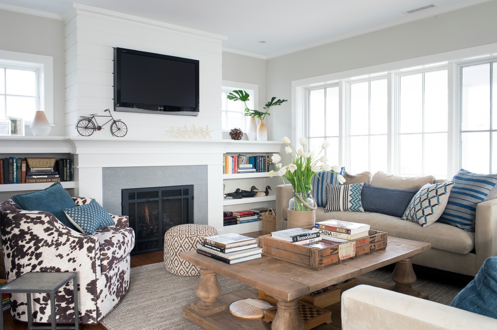 Design ideas for a mid-sized beach style open concept living room in New York with grey walls, a standard fireplace, a wall-mounted tv, a library, medium hardwood floors, a concrete fireplace surround and brown floor.