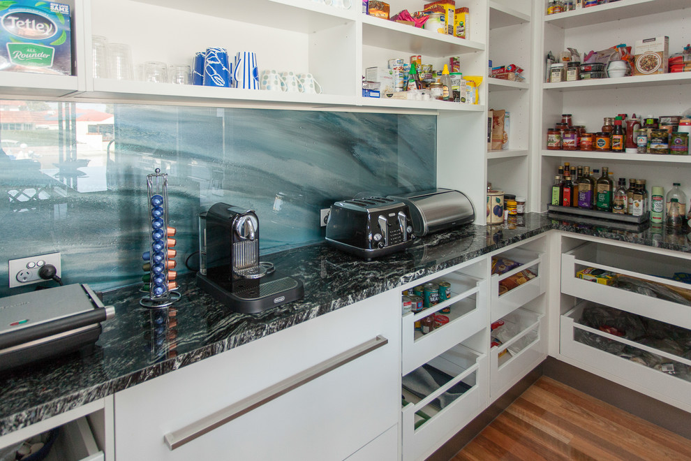 Contemporary kitchen pantry in Gold Coast - Tweed with an undermount sink, flat-panel cabinets, white cabinets, marble benchtops, blue splashback, glass sheet splashback, stainless steel appliances, medium hardwood floors and with island.