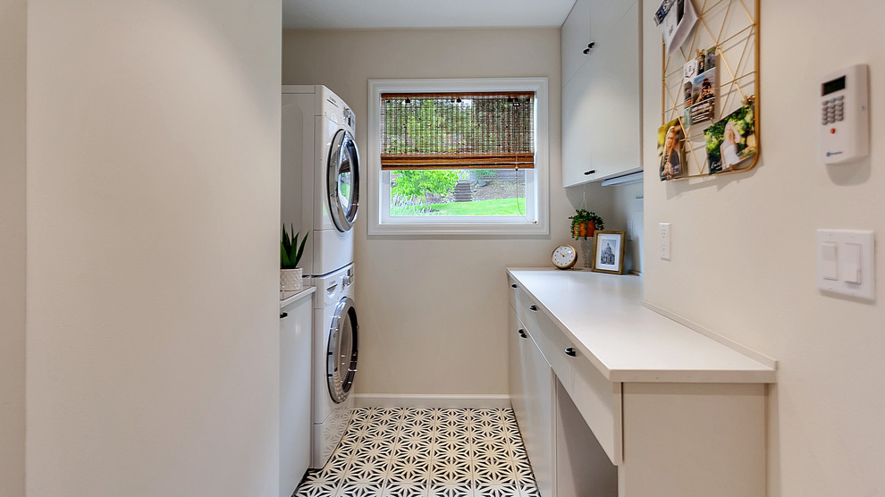 Photo of a small midcentury galley utility room in Portland with flat-panel cabinets, grey cabinets, quartz benchtops, grey walls, ceramic floors, a stacked washer and dryer, blue floor and grey benchtop.