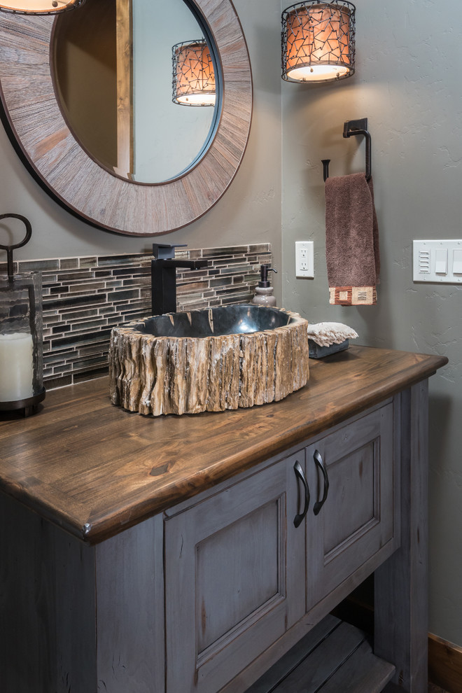 Photo of a small country 3/4 bathroom in Other with beaded inset cabinets, distressed cabinets, multi-coloured tile, glass tile, grey walls, a vessel sink and wood benchtops.