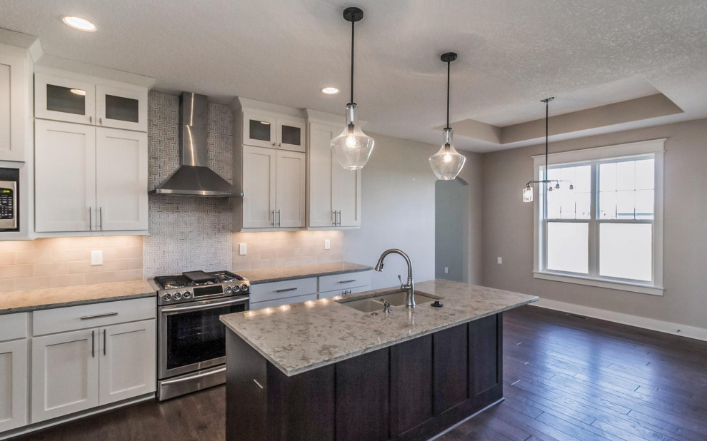 Example of a transitional l-shaped medium tone wood floor and brown floor eat-in kitchen design with an undermount sink, shaker cabinets, white cabinets, quartz countertops, ceramic backsplash, stainless steel appliances and an island