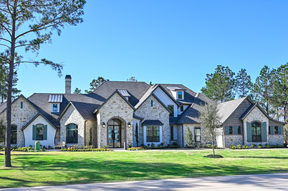 This is an example of a large two-storey brown house exterior in Houston with stone veneer, a shingle roof, a black roof and shingle siding.