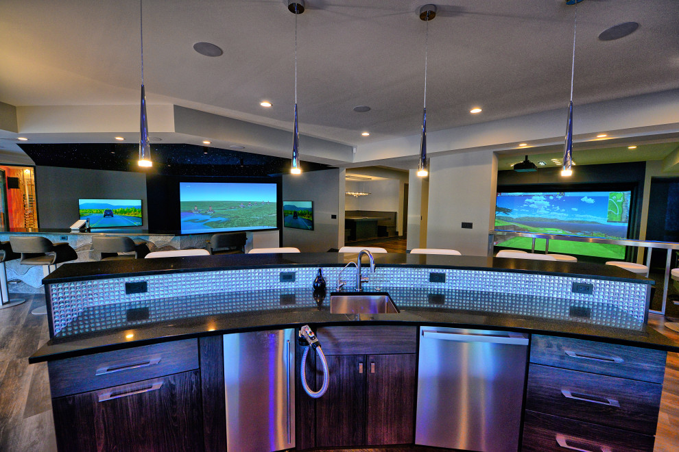 This is an example of a large modern u-shaped seated home bar in Indianapolis with an undermount sink, flat-panel cabinets, grey cabinets, quartz benchtops, blue splashback, glass tile splashback, porcelain floors, grey floor and black benchtop.