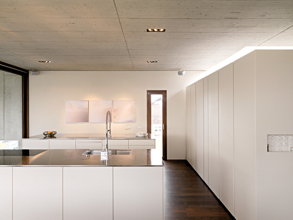 Design ideas for a large contemporary separate kitchen in Stuttgart with flat-panel cabinets, white cabinets, an integrated sink, stainless steel benchtops, panelled appliances, dark hardwood floors and multiple islands.