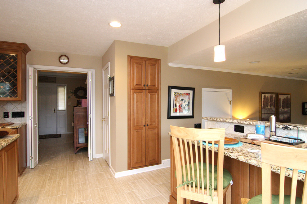 Large transitional u-shaped porcelain tile eat-in kitchen photo with an undermount sink, raised-panel cabinets, medium tone wood cabinets, granite countertops, beige backsplash, porcelain backsplash and stainless steel appliances