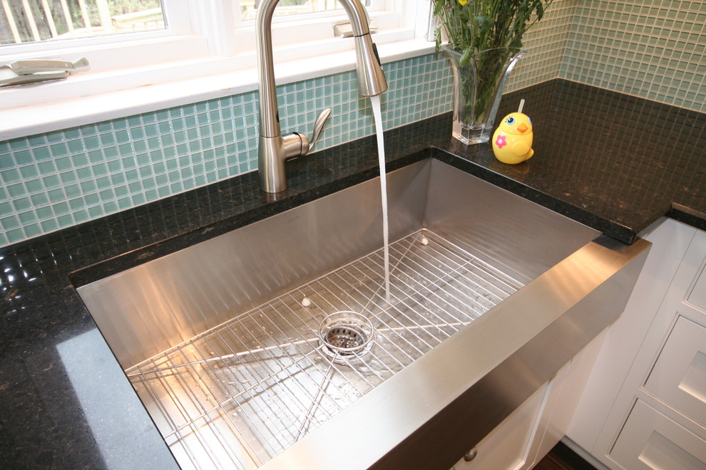 Enclosed kitchen - mid-sized transitional u-shaped porcelain tile and brown floor enclosed kitchen idea with a farmhouse sink, shaker cabinets, white cabinets, quartzite countertops, green backsplash, glass tile backsplash, white appliances, an island and black countertops