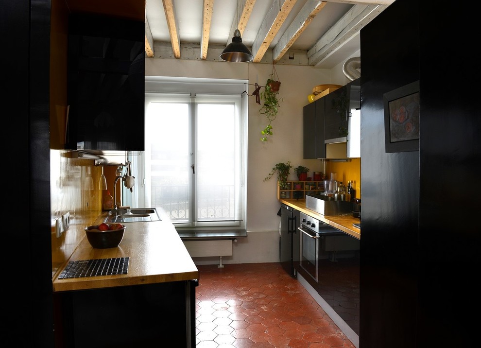 Photo of a mid-sized contemporary galley separate kitchen in Paris with a double-bowl sink, flat-panel cabinets, black cabinets, wood benchtops, yellow splashback, panelled appliances, terra-cotta floors and no island.