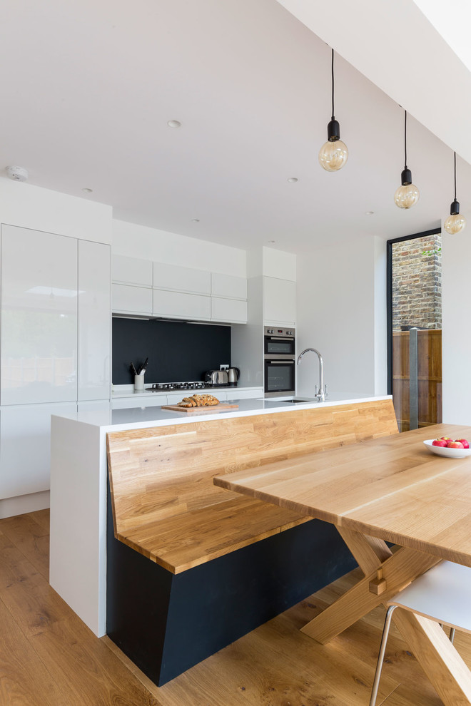This is an example of a large contemporary galley open plan kitchen in London with flat-panel cabinets, white cabinets, quartzite benchtops, panelled appliances, medium hardwood floors and with island.