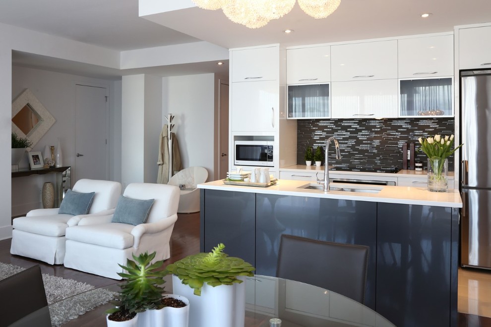 This is an example of a mid-sized modern single-wall open plan kitchen in Montreal with an undermount sink, flat-panel cabinets, white cabinets, quartz benchtops, black splashback, matchstick tile splashback, stainless steel appliances, medium hardwood floors, with island and brown floor.