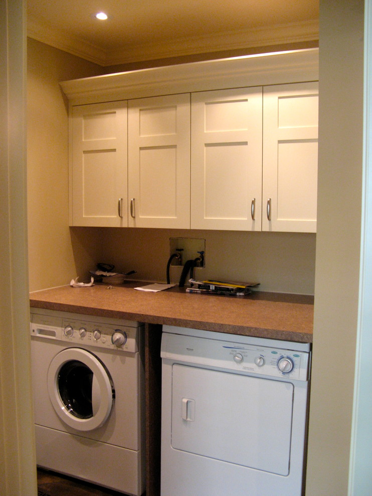 Small traditional galley utility room in Calgary with shaker cabinets, white cabinets, laminate benchtops, beige walls, ceramic floors and a side-by-side washer and dryer.