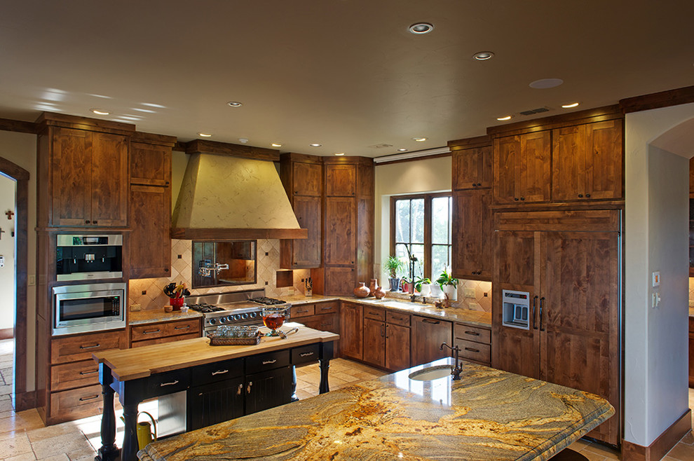 Inspiration for a mid-sized traditional l-shaped separate kitchen in Dallas with a farmhouse sink, shaker cabinets, dark wood cabinets, marble benchtops, beige splashback, stone tile splashback, stainless steel appliances, limestone floors, multiple islands, beige floor and brown benchtop.