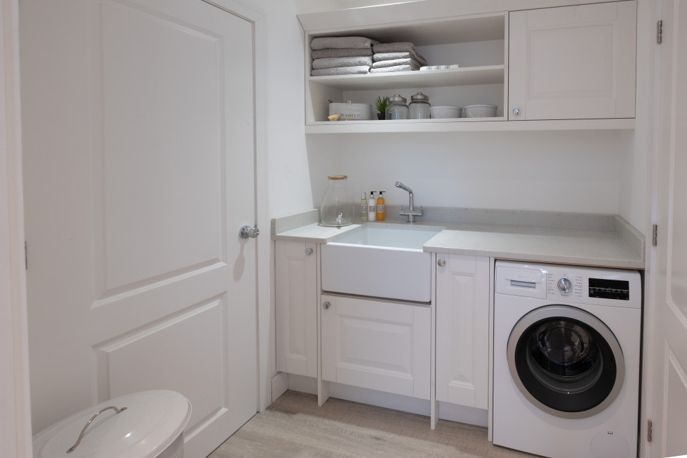 This is an example of a medium sized beach style utility room in Hampshire with white cabinets, quartz worktops, white walls, laminate floors, grey floors and white worktops.