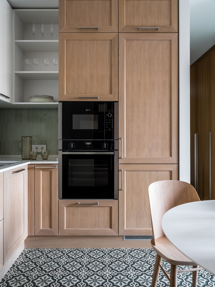 Small contemporary l-shaped eat-in kitchen in Moscow with a single-bowl sink, raised-panel cabinets, light wood cabinets, quartz benchtops, green splashback, ceramic splashback, black appliances, porcelain floors, green floor and white benchtop.