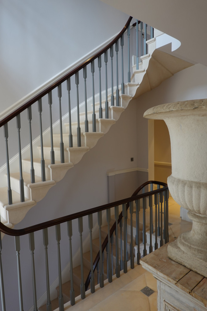 На фото: изогнутая лестница с ступенями из известняка, подступенками из известняка и деревянными перилами с