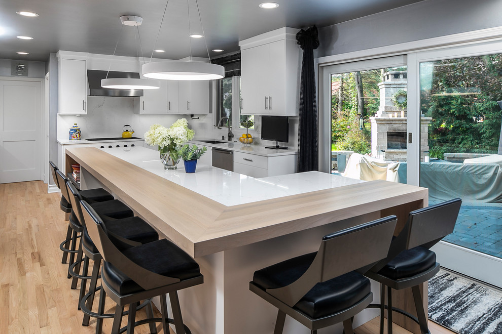 Large contemporary l-shaped eat-in kitchen in Detroit with an undermount sink, flat-panel cabinets, white cabinets, quartz benchtops, white splashback, stone slab splashback, stainless steel appliances, medium hardwood floors, with island, brown floor and white benchtop.