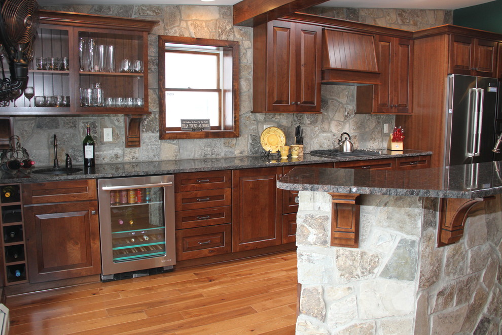 Photo of a mid-sized country single-wall eat-in kitchen in New York with an undermount sink, raised-panel cabinets, medium wood cabinets, granite benchtops, multi-coloured splashback, stainless steel appliances, light hardwood floors and with island.
