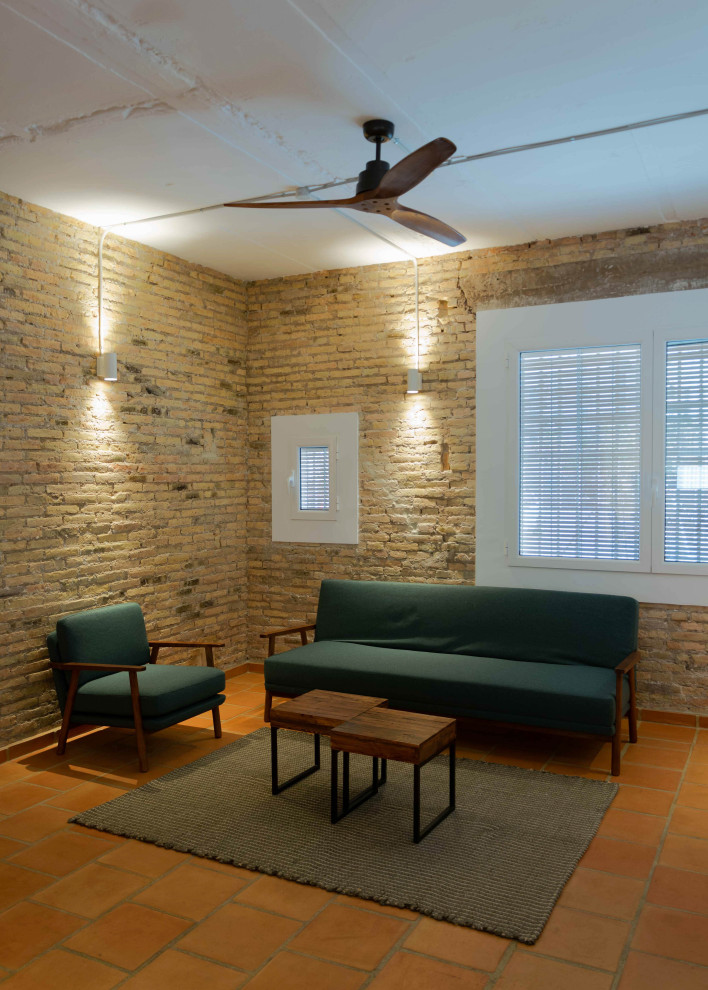 На фото: открытая гостиная комната среднего размера в средиземноморском стиле с коричневыми стенами, полом из терракотовой плитки, телевизором на стене, коричневым полом и кирпичными стенами с
