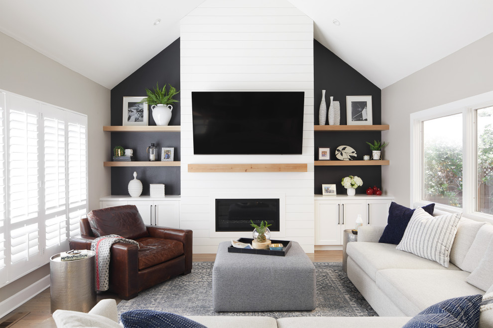 Photo of a transitional living room in San Francisco with black walls, light hardwood floors, a wood fireplace surround, a wall-mounted tv, beige floor and vaulted.