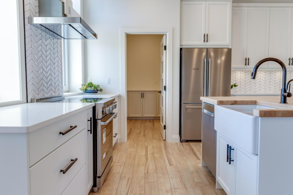 Large farmhouse u-shaped light wood floor, beige floor and vaulted ceiling eat-in kitchen photo in Other with a farmhouse sink, shaker cabinets, white cabinets, quartzite countertops, white backsplash, subway tile backsplash, stainless steel appliances, an island and white countertops