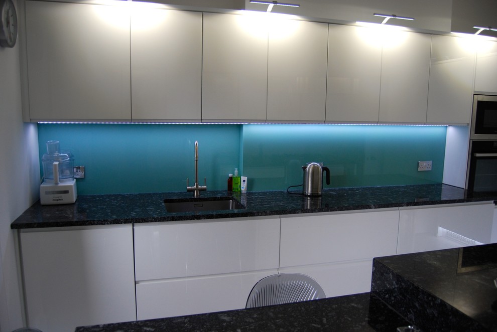 Inspiration for a large modern l-shaped eat-in kitchen in Glasgow with a drop-in sink, flat-panel cabinets, white cabinets, granite benchtops, blue splashback, glass sheet splashback, stainless steel appliances, porcelain floors and with island.
