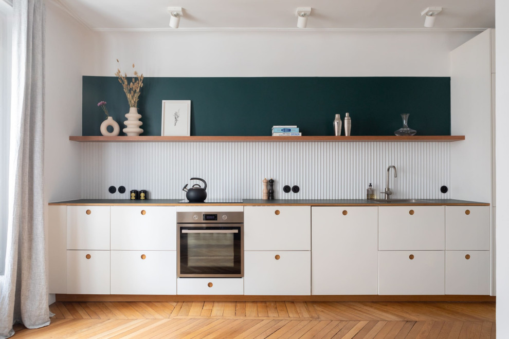 Photo of a large scandinavian single-wall open plan kitchen in Paris with light wood cabinets, no island, an integrated sink, white splashback, panelled appliances, medium hardwood floors and brown floor.