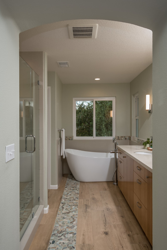 This is an example of a large contemporary master bathroom in San Francisco with flat-panel cabinets, light wood cabinets, a freestanding tub, an alcove shower, a two-piece toilet, beige tile, porcelain tile, green walls, porcelain floors, an undermount sink and engineered quartz benchtops.