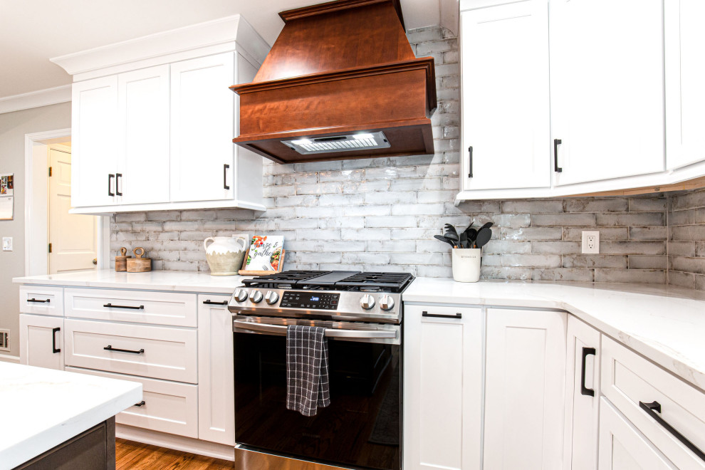 Inredning av ett lantligt avskilt, mellanstort vit vitt u-kök, med en undermonterad diskho, skåp i shakerstil, vita skåp, bänkskiva i kvarts, grått stänkskydd, stänkskydd i tunnelbanekakel, rostfria vitvaror, mellanmörkt trägolv, en köksö och brunt golv
