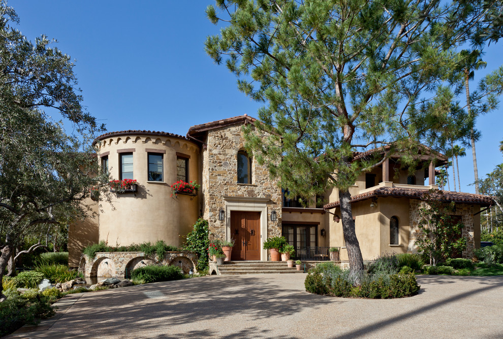 This is an example of a large mediterranean two-storey beige exterior in Los Angeles with stone veneer and a gambrel roof.