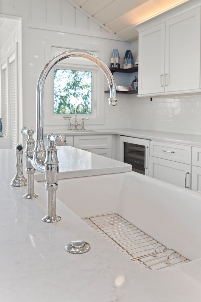 Photo of a large beach style u-shaped open plan kitchen in Milwaukee with a farmhouse sink, shaker cabinets, white cabinets, quartz benchtops, white splashback, subway tile splashback, stainless steel appliances, dark hardwood floors, with island, brown floor, white benchtop and wood.