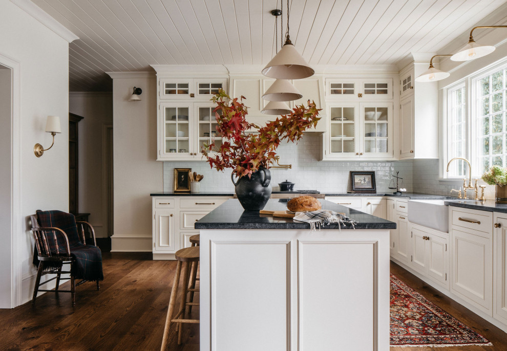 This is an example of a classic kitchen in Chicago with a belfast sink, white cabinets, white splashback, an island, a timber clad ceiling and glass-front cabinets.