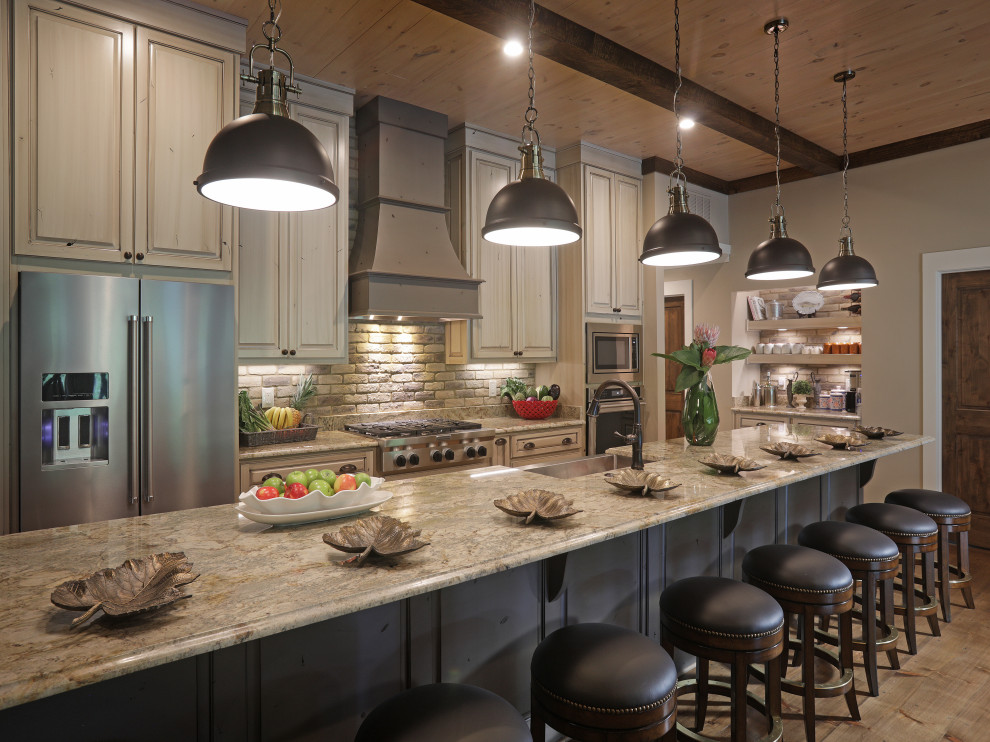 This is an example of a country galley kitchen in Atlanta with a farmhouse sink, raised-panel cabinets, light wood cabinets, grey splashback, stainless steel appliances, medium hardwood floors, with island, brown floor, beige benchtop and wood.