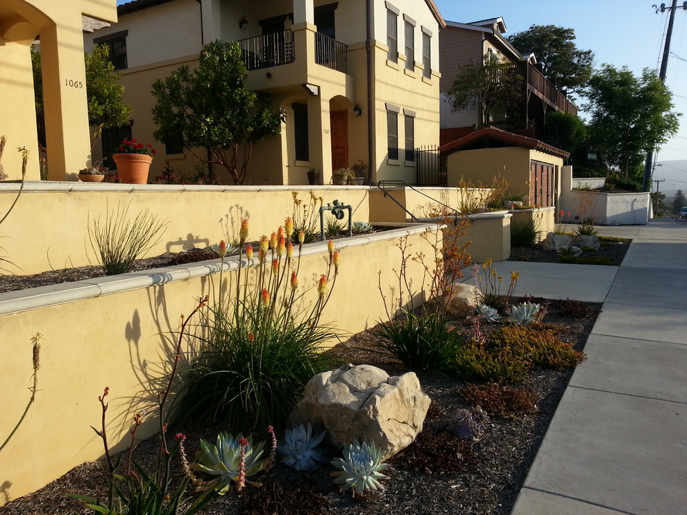 Inspiration for a mid-sized mediterranean front yard partial sun driveway for summer in San Luis Obispo with a retaining wall and concrete pavers.