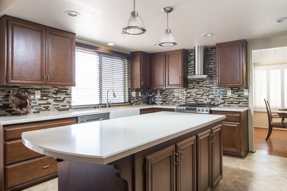 Large transitional u-shaped eat-in kitchen in Los Angeles with a farmhouse sink, raised-panel cabinets, dark wood cabinets, quartz benchtops, multi-coloured splashback, glass tile splashback, stainless steel appliances, cement tiles, with island, beige floor and white benchtop.